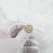 Gloved hand holding and rotating a sparkling gold iced-out round signet ring.