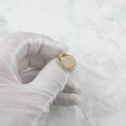 White-gloved hand displaying a gold round signet ring paved with cubic zirconia