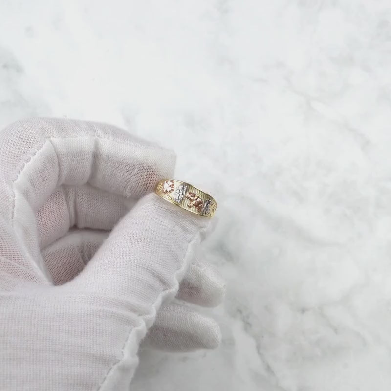 Gloved hand holding the tricolor gold lucky motif ring against a light background.