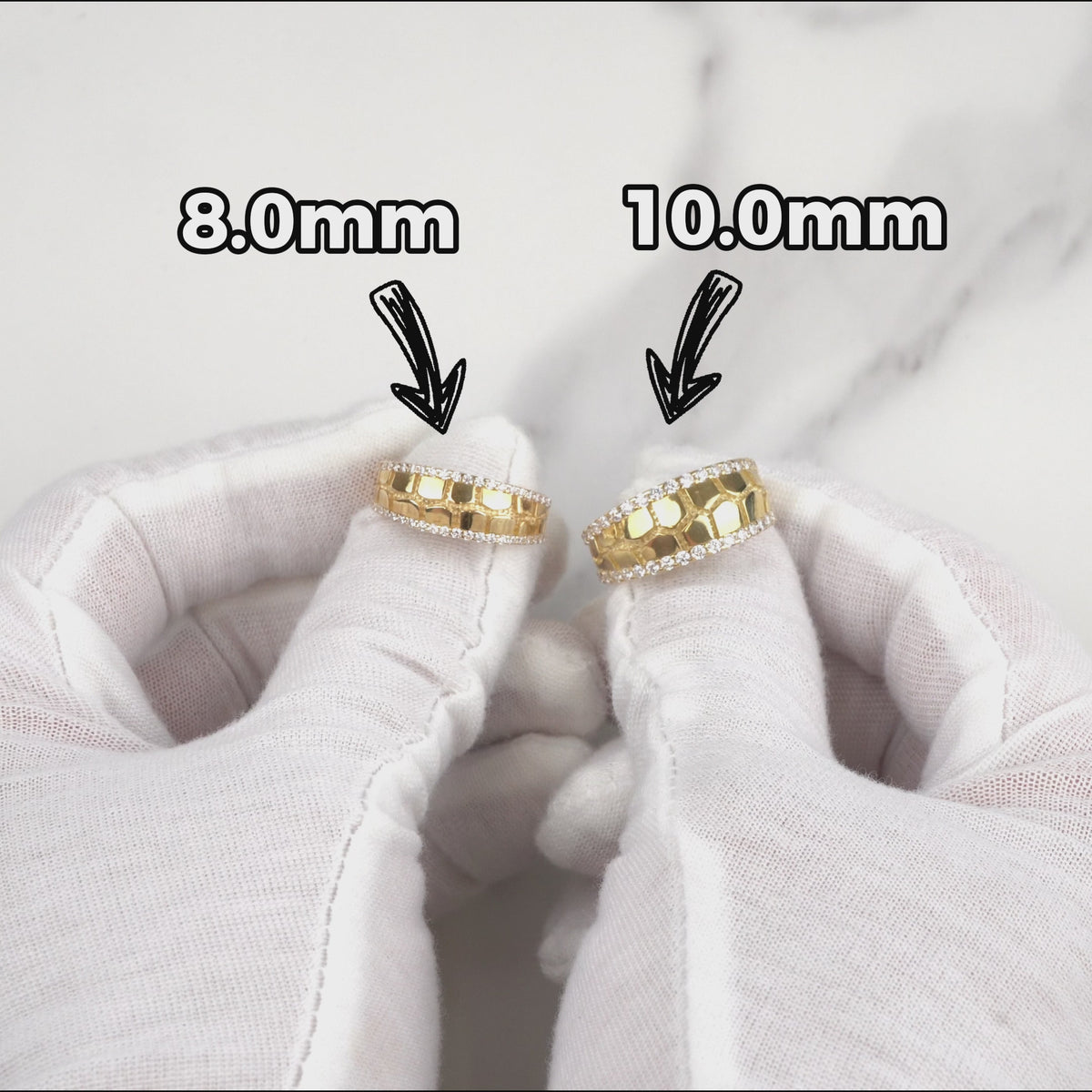 Gloved hands holding 8.0mm and 10.0mm gold classic nugget band rings.