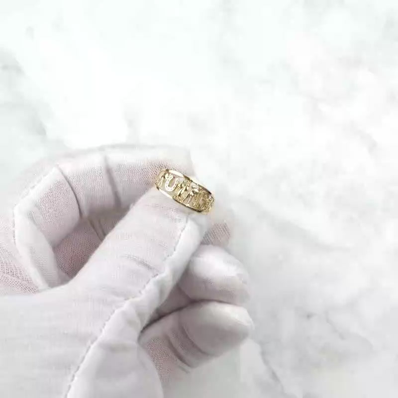 Gloved hand holding up the polished yellow gold lucky motif ring.