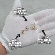 Three labeled sizes of gold Quinceañera royal crown pendants resting on a white gloved hand.