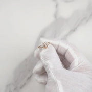Gloved hand holding a gold Virgin Mary CZ ring over a marble background.