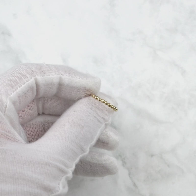 Video showcase of a delicate yellow gold beaded thin band ring spinning slowly.
