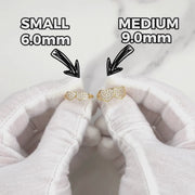 Gloved hands holding small and medium gold dual-heart cubic zirconia rings.