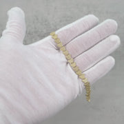Gloved hand displaying a 10k yellow gold butterfly link bracelet over gray background.