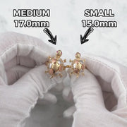 Hands wearing white gloves holding medium and small gold turtle locket rings for size comparison.